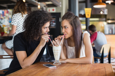 Young couple looking at each other while having drink together at table in restaurantの写真素材