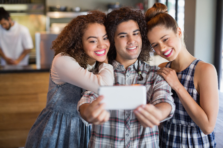 Young man taking selfie with female friends in cafeの写真素材