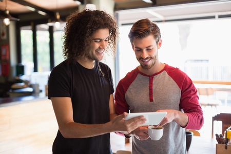 Happy young friend using digital tablet while standing in restaurantの写真素材