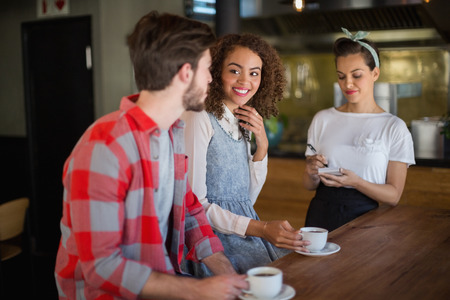 Smiling woman looking at friend while placing order to waitress in restaurantの写真素材
