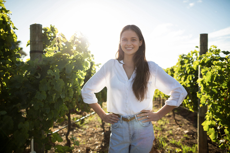 Portrait of smiling woman with hand on hip standing at vineyardの写真素材