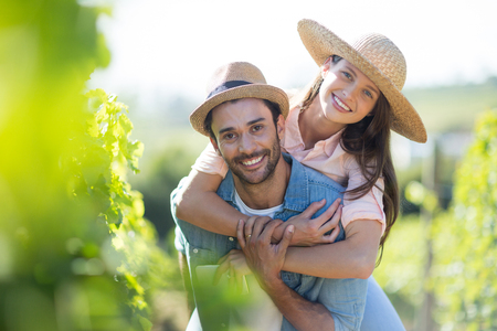 Portrait of smiling couple piggybacking at vineyard during sunny dayの写真素材