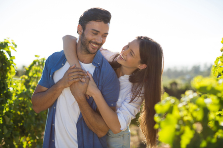 Cheerful couple embracing at vineyard against sky during sunny dayの写真素材