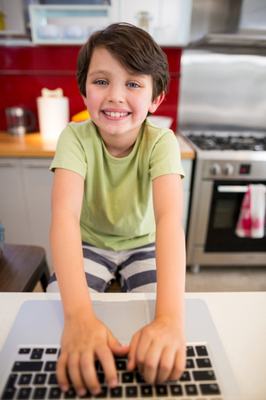 Portrait of smiling boy using laptop in kitchen at homeの写真素材