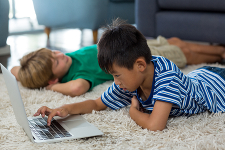 Boy lying on rug and using laptop in living room at home