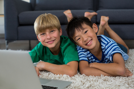 Portrait of smiling siblings with laptop lying on rugの写真素材