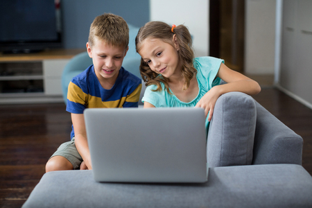 Smiling siblings using laptop in living room at homeの写真素材