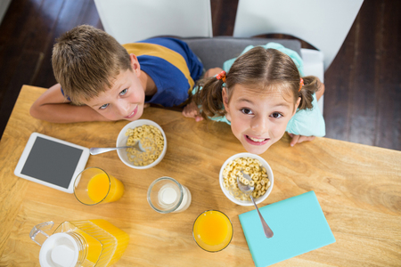 Portrait of smiling sibling having breakfast cereal in kitchen at homeの写真素材