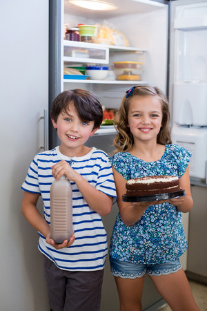Portrait of siblings holding cake and bottle in kitchenの写真素材