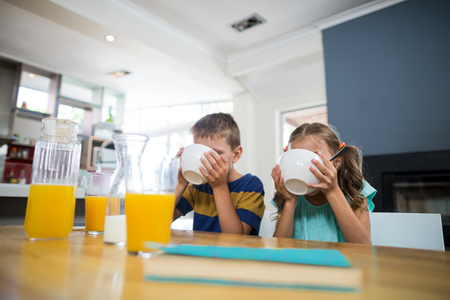Sibling having breakfast cereal in kitchen at homeの写真素材