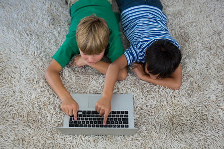 Siblings lying on rug and using laptop in living room at homeの写真素材