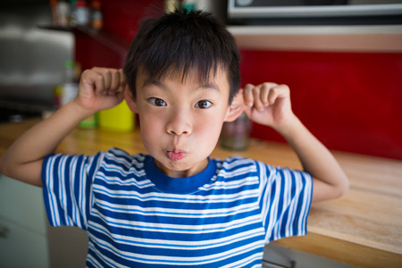 Boy making funny face in kitchen at homeの写真素材