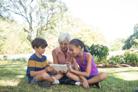 Grandmother and grand kids using digital tablet in the park on sunny dayの写真素材