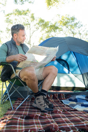 Man reading the map outside the tent at campsiteの写真素材