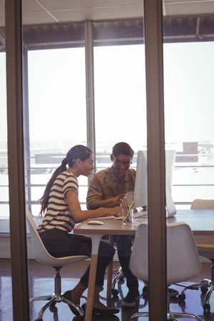 Businessman working with female colleague seen through glass in officeの写真素材