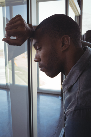 Close up of tired businessman leaning on glass in officeの写真素材