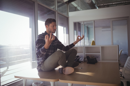 Businessman meditating on table by glass window at officeの写真素材