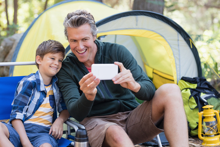 Happy father and son taking selfie by tent in forestの写真素材