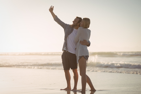 Young couple taking selfie on shore at beach during sunny dayの写真素材