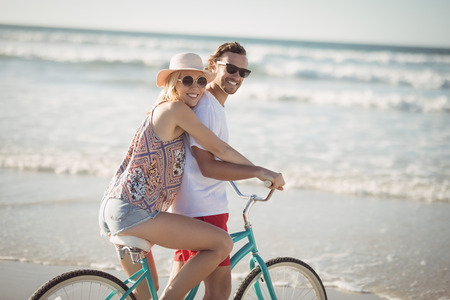 Smiling couple riding bicycle at beach during sunny dayの写真素材