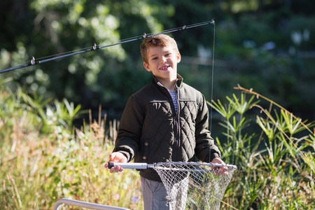 Portrait of smiling boy holding fishing net while standing in forest on sunny dayの写真素材
