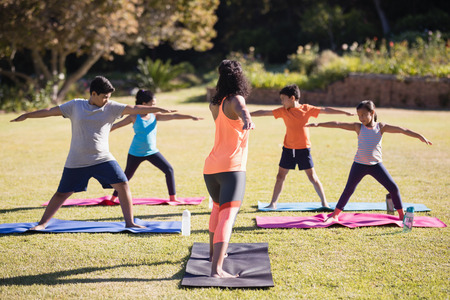 Female instructor teaching kids Virabhadrasana II on mat at parkの写真素材