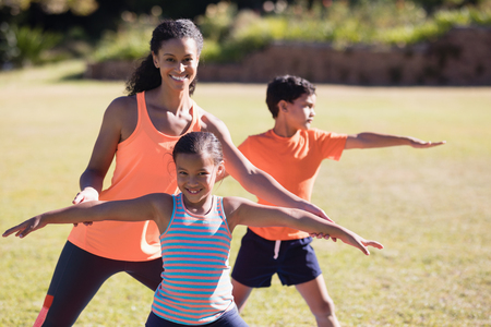 Portrait of happy female trainer and girl practicing Virabhadrasana II pose at parkの写真素材