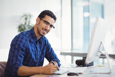 Portrait of smiling graphic designer using graphic tablet at desk in officeの写真素材