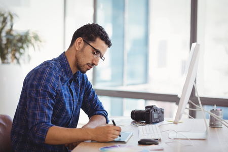 Graphic designer using graphic tablet at desk in officeの写真素材