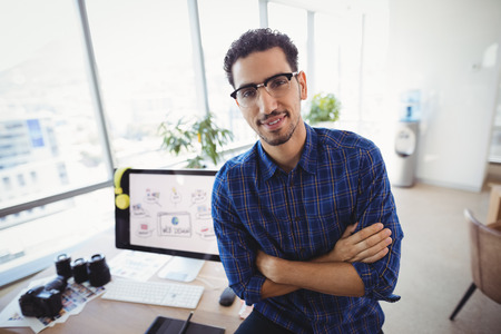 Portrait of graphic designer standing with arms crossed at desk in office