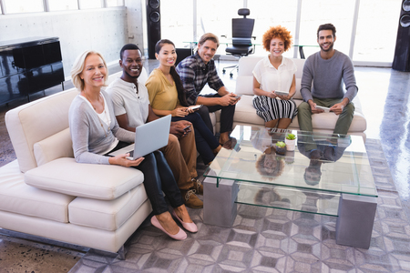 Portrait of smiling colleagues sitting on sofa in officeの写真素材