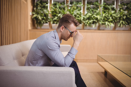 Tensed executive sitting on sofa in officeの写真素材