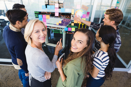 Portrait of business people standing by plan on glass wall in officeの写真素材