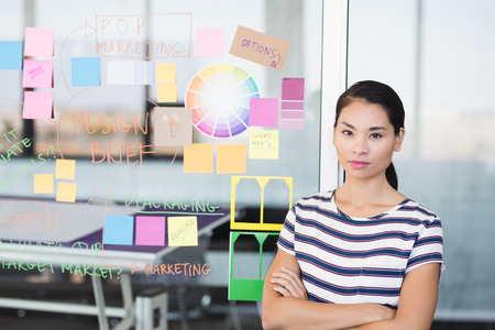 Portrait of confident businesswoman standing by plan on glass wall in office