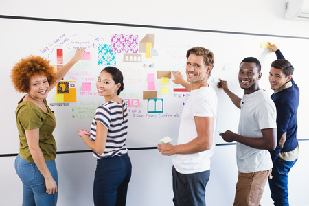 Portrait of business people sticking adhesive note during planning in officeの写真素材