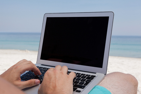 Mid section of man using laptop while resting on chair at beachの写真素材