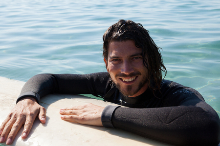 Portrait of smiling surfer leaning on surfboard in sea