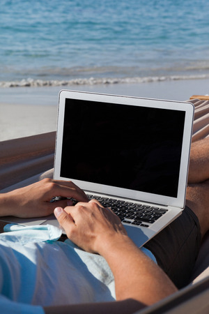 Man using laptop while relaxing on hammock in beachの写真素材