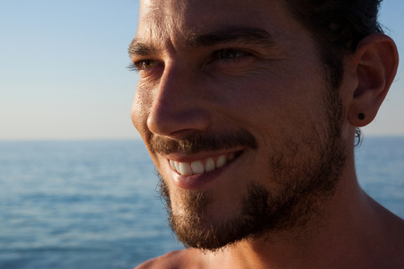 Close up of smiling man looking away at beach during sunny dayの写真素材