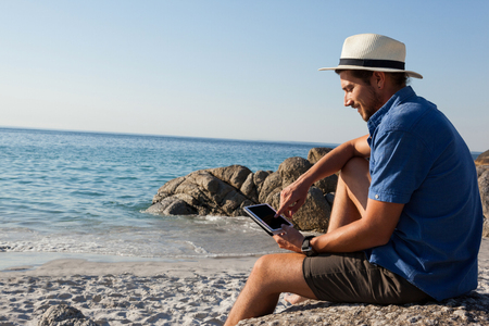 Smiling man using digital tablet on the beach on a sunny dayの写真素材