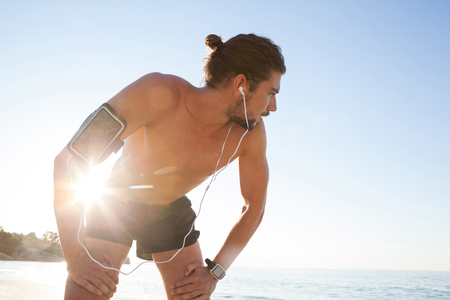 Exhausted man taking a break after jogging on beach on a sunny dayの写真素材