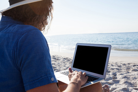 Man using laptop on the beach on a sunny dayの写真素材