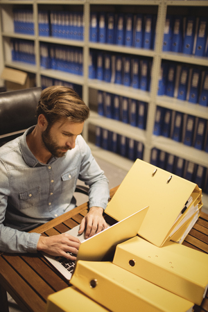 High angle view of businessman using laptop by files on table in storage roomの写真素材