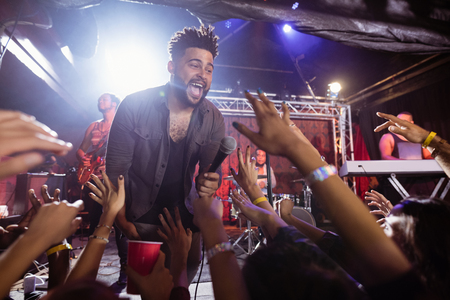 Young male singer performing on stage by crowd at nightclub during music festivalの写真素材