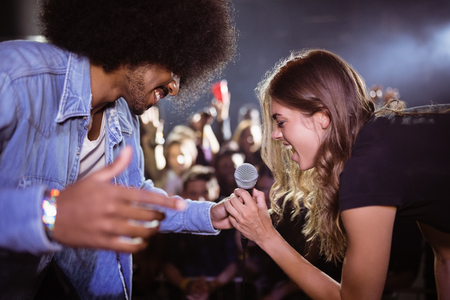 Cheerful woman singing with male singer at nightclub during music festival