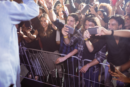 Cheerful fans photographing performer at nightclub during music festivalの写真素材