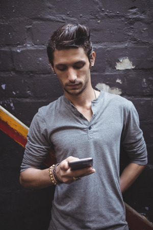 Young man using mobile phone against wallの写真素材