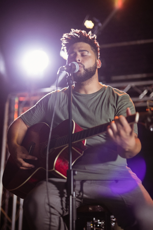 Male musician with eyes closed singing on stage at nightclubの写真素材