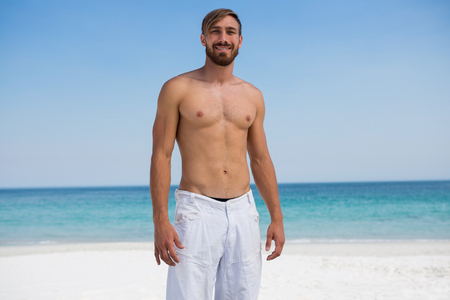 Portrait of smiling shirtless man standing at beach against skyの写真素材