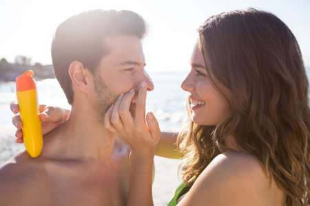 Smiling woman applying sunscream on man face at beach on sunny dayの写真素材